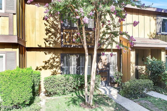 Front view of a two-story house with wood paneling and surrounding greenery.