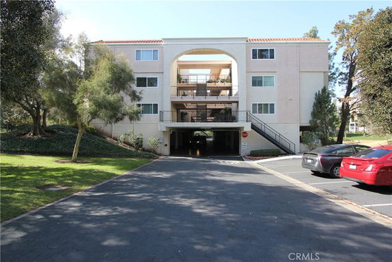 Front view of a multi-story building with balconies and parking on the ground level.