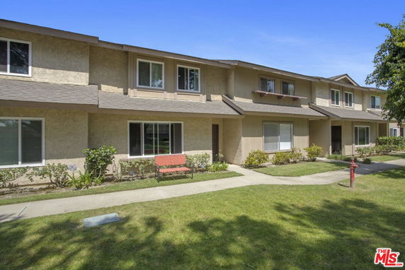 Front view of a two-story residential building with multiple windows and doors, featuring a small lawn and a bench in the front.