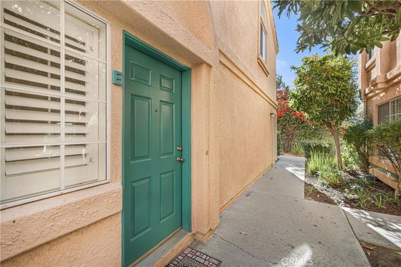 Front view of a building entrance with a teal door and adjacent window, surrounded by stucco walls.
