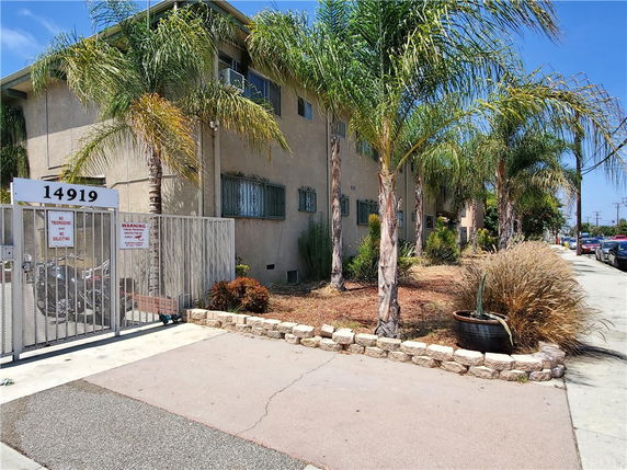 Front view of a multi-story building with gated entrance and palm trees.