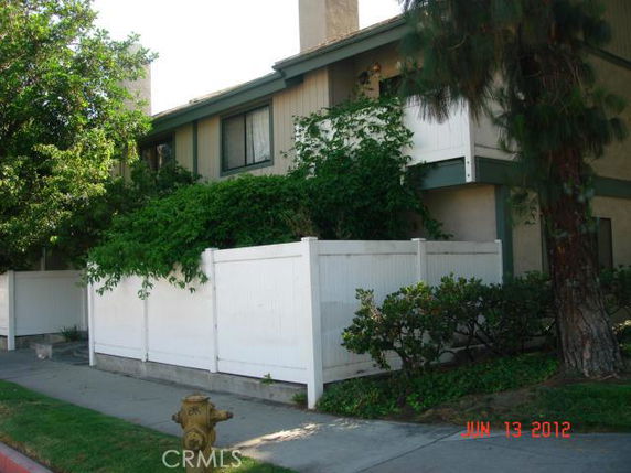 Front view of a two-story residential building with a white fence and greenery.