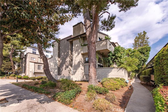Front view of a multi-story building with trees and shrubs surrounding it.