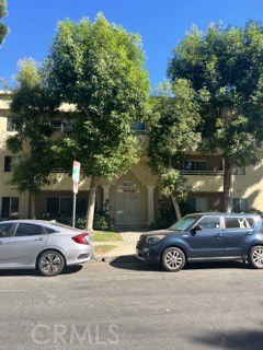 Front view of a multi-story residential building with trees and parked cars.