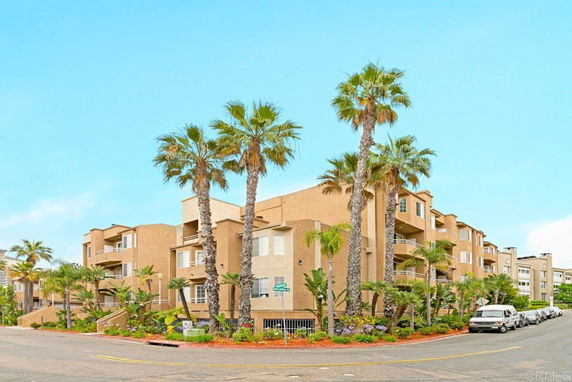 Front view of a multi-story apartment building with balconies and palm trees.
