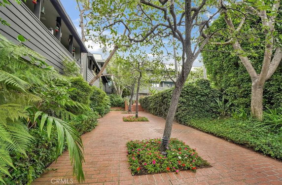 Pathway with trees and plants beside a building with balconies.