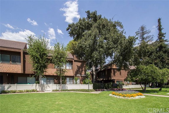 Front view of a two-story building with brown siding and a fence, surrounded by trees and landscaping.