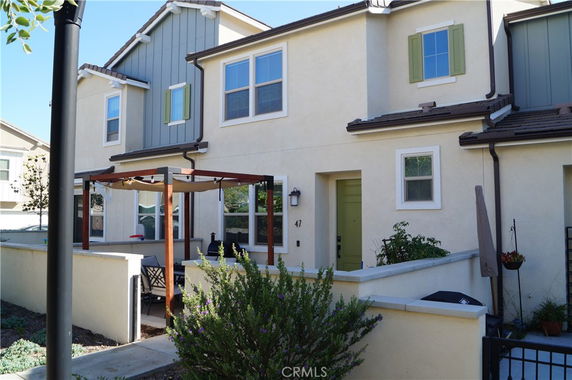 Front view of a two-story house with a small patio and pergola.