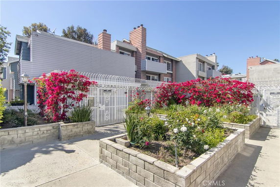 Front view of a multi-story building with a gated entrance and colorful flowers.