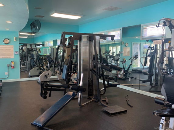 Indoor gym area with various exercise equipment and mirrors on the walls.