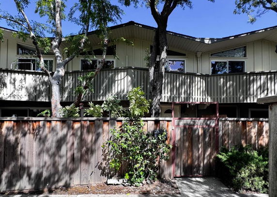Front view of a two-story building with a wooden fence and trees in front.