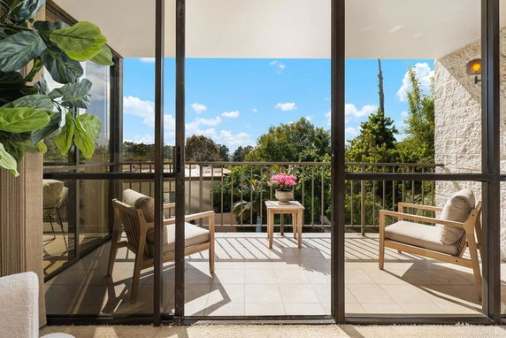 View from a balcony with chairs and a table, overlooking greenery and a blue sky.