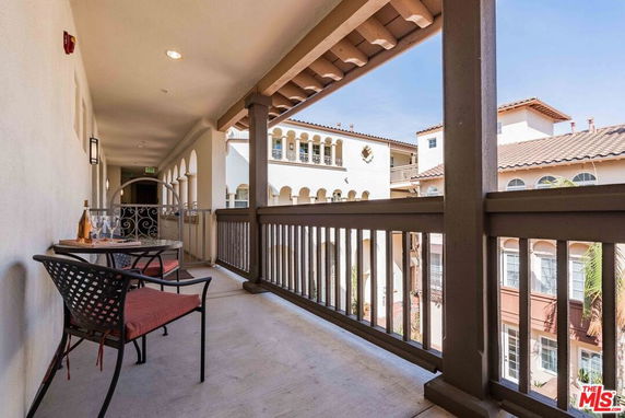 View from a covered balcony overlooking surrounding buildings with arch windows and tile roofs.