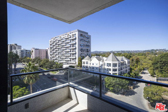 Panoramic view from a balcony overlooking multiple residential buildings and a tree-lined street.