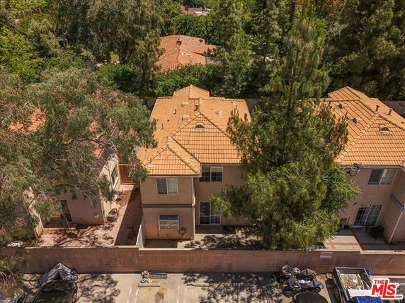 Aerial view of the rooftops of several two-story residential buildings with light red tiles surrounded by trees.