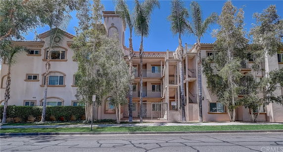 Front view of a multi-story apartment building with a central entrance and surrounded by palm trees.
