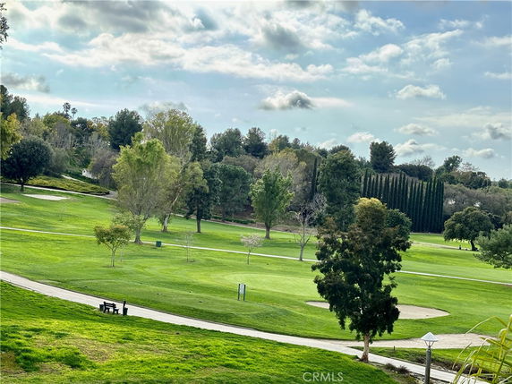 View of a golf course with green grass, trees, and a cloudy sky in the background.
