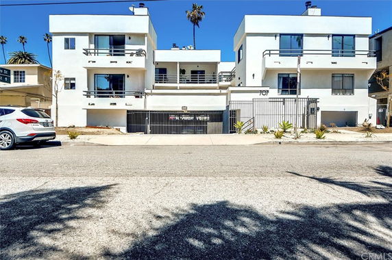 Front view of a modern multi-story apartment building with balconies and gated entrance.