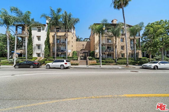 Front view of a multi-story residential building with palm trees and parked cars.