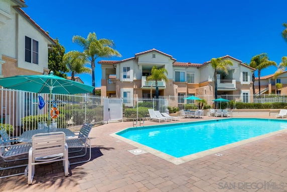 Outdoor swimming pool area in front of a two-story residential building complex.