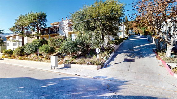 Front view of a multi-story residential building surrounded by trees and bushes.