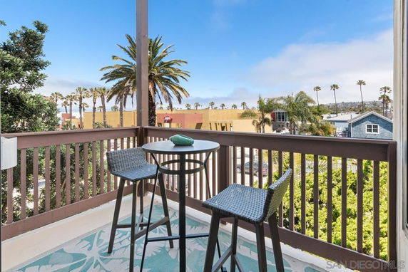Panoramic view from a balcony with outdoor seating overlooking palm trees and cityscape.
