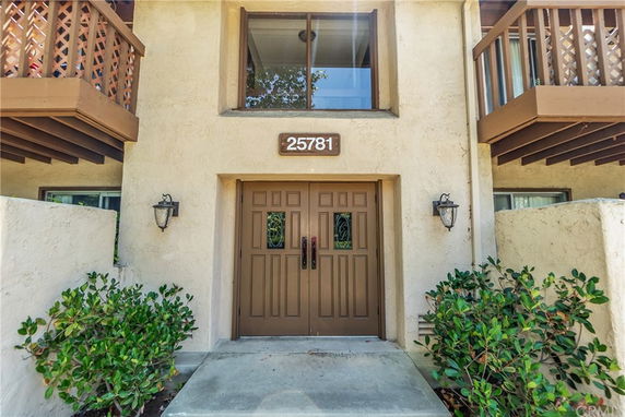 Front view of a two-story building entrance with a brown door and adjacent balconies.