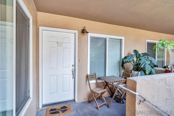 Outdoor entrance area with a white door, two chairs, a small table, and potted plants.
