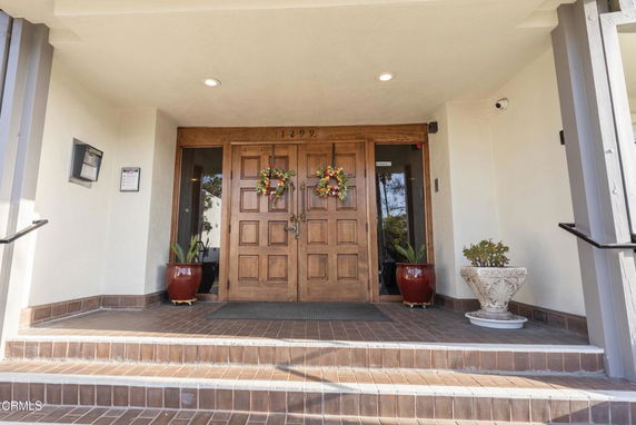 Front view of an entrance with wooden double doors and potted plants.
