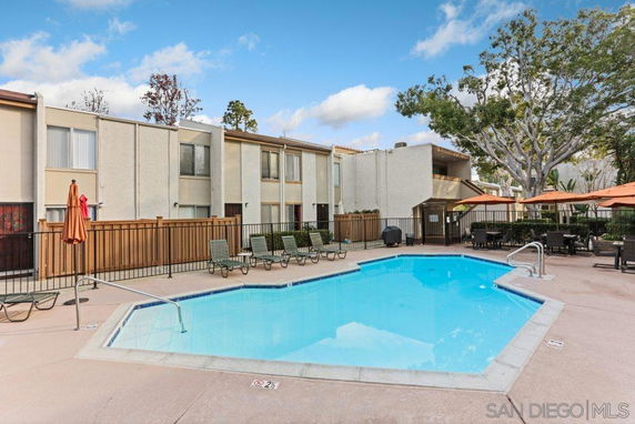 Outdoor swimming pool area with seating and umbrellas in front of a multi-story residential building.