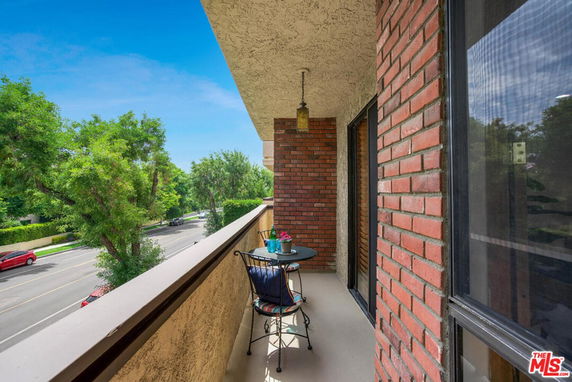 Balcony view of a residential area with a small table and chair set, overlooking trees and a street.