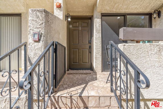 Front view of a house entrance with stairs and metal railings leading to a brown door.