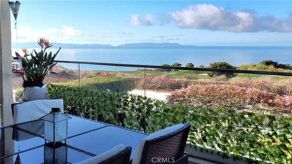 Balcony view overlooking the ocean with mountains in the distance and lush greenery below.
