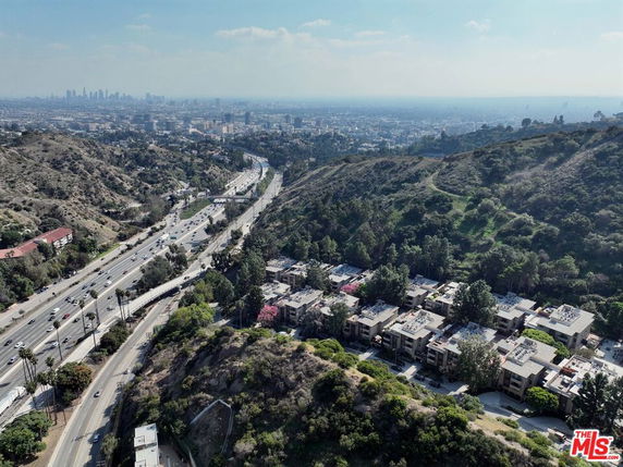 Panoramic view over a highway and residential area with hills and city skyline in the background.