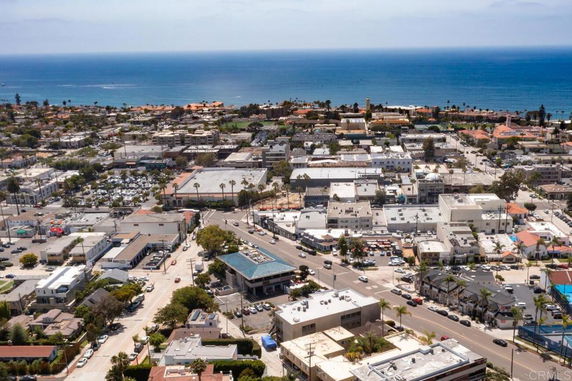 Wide aerial view of a coastal town with multiple buildings and the ocean in the background.
