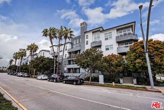 Front view of a multi-story residential building with balconies and palm trees along the street.