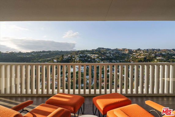 Panoramic view from a building balcony overlooking a hilly landscape with houses.