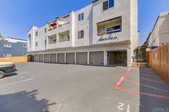 Outdoor parking area in front of a multi-story building with garages.