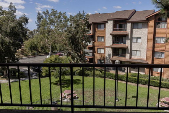 View from a balcony overlooking a residential area with a multi-story building and greenery.