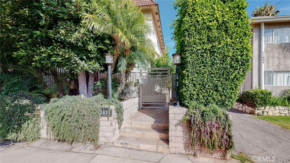 Front view of a residential entrance with gate and surrounding greenery.