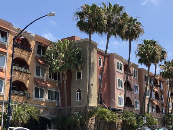 Front view of a multi-story residential building with balconies and palm trees.