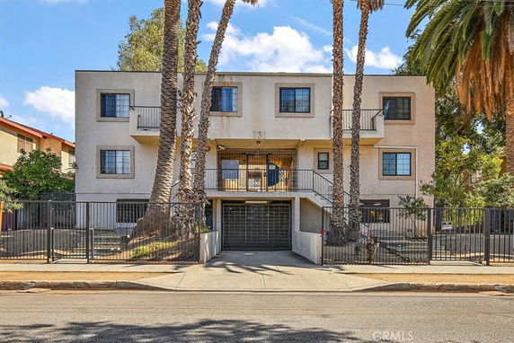 Front view of a multi-story apartment building with balconies and a gated entrance.