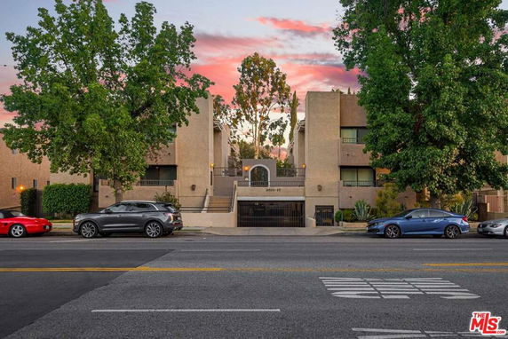 Front view of a multi-story residential building with a central entrance and surrounding trees.