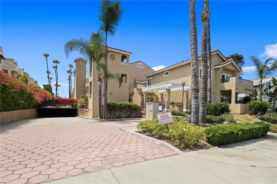 Front view of a multi-story building with palm trees and a gated entrance.