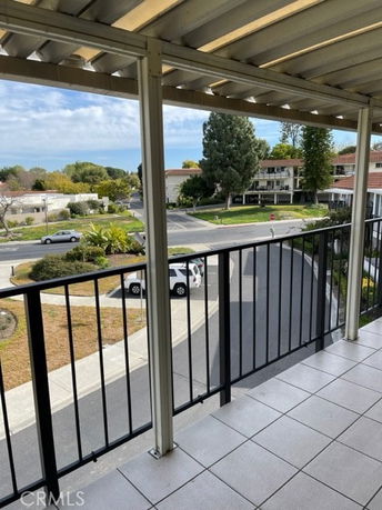 View from a covered balcony overlooking a suburban street with trees and buildings.