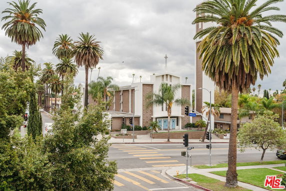 Front view of a building with a cross on top and palm trees around.