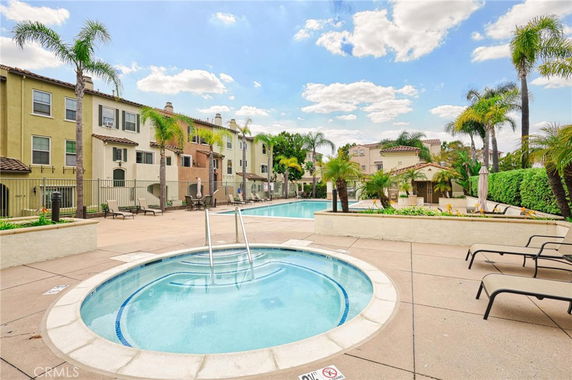 Outdoor swimming pool area with surrounding buildings and palm trees.