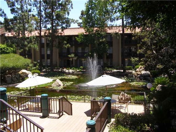 View of the garden area with a pond and fountain in front of a multi-story building.
