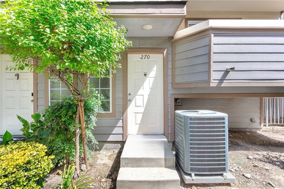 Front view of a house with a white door and window, featuring a tree and air conditioning unit outside.
