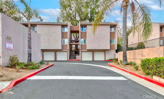 Front view of a residential building with two garage doors and palm trees lining the driveway.